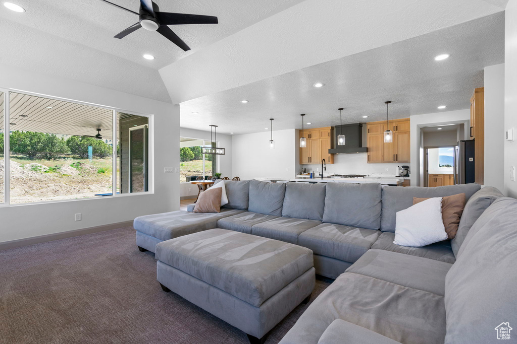 Carpeted living room with vaulted ceiling, sink, and ceiling fan