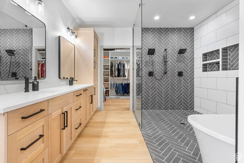 Bathroom with shower with separate bathtub, wood-type flooring, vanity, and tile walls