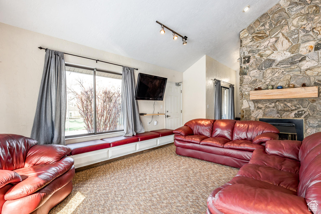 Carpeted living room featuring vaulted ceiling, a stone fireplace, a textured ceiling, and rail lighting