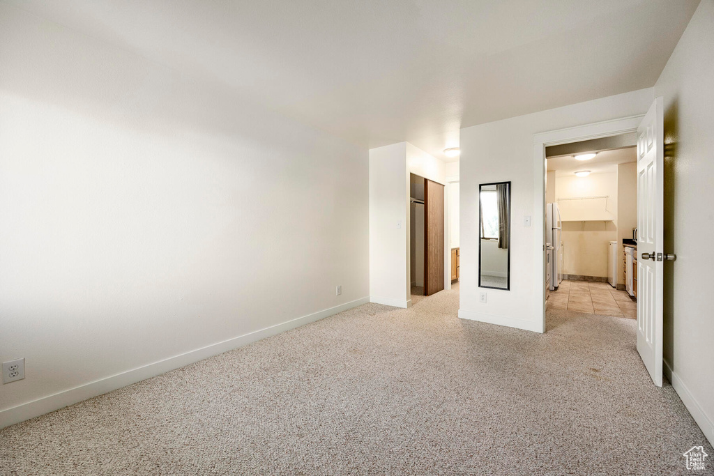 Unfurnished bedroom featuring light colored carpet, a closet, and fridge