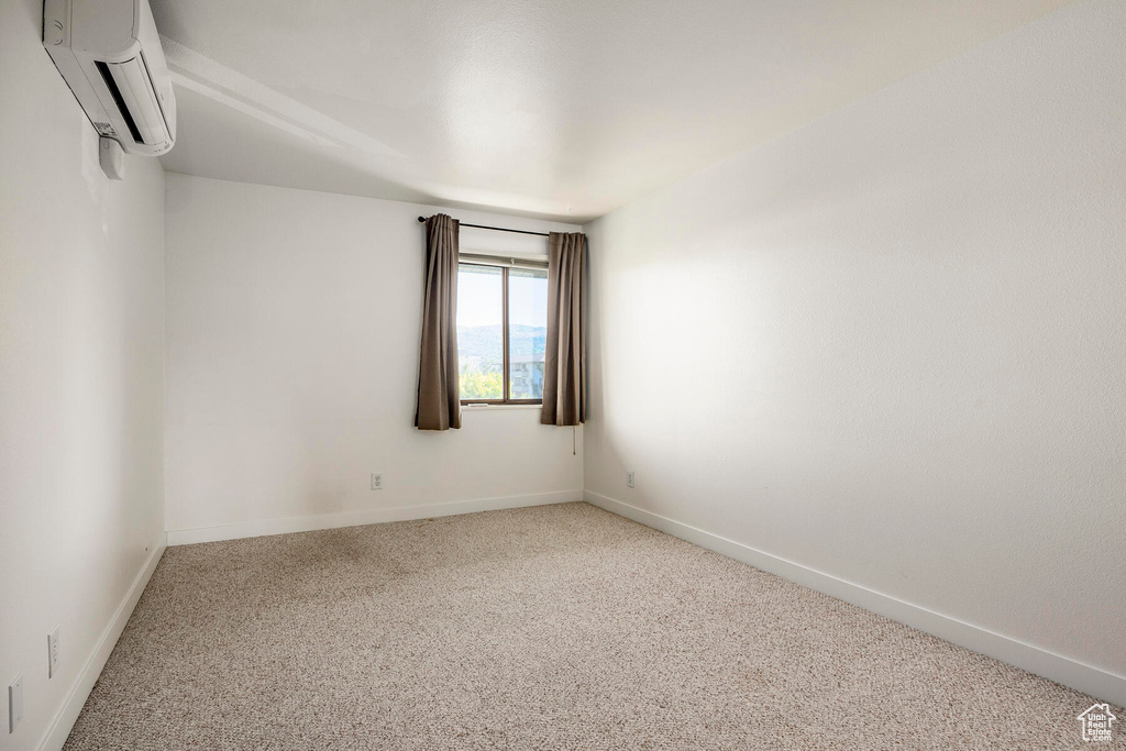 Empty room featuring carpet flooring and an AC wall unit