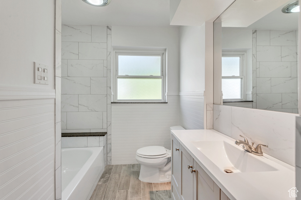 Bathroom with tile walls, oversized vanity, toilet, and wood-type flooring