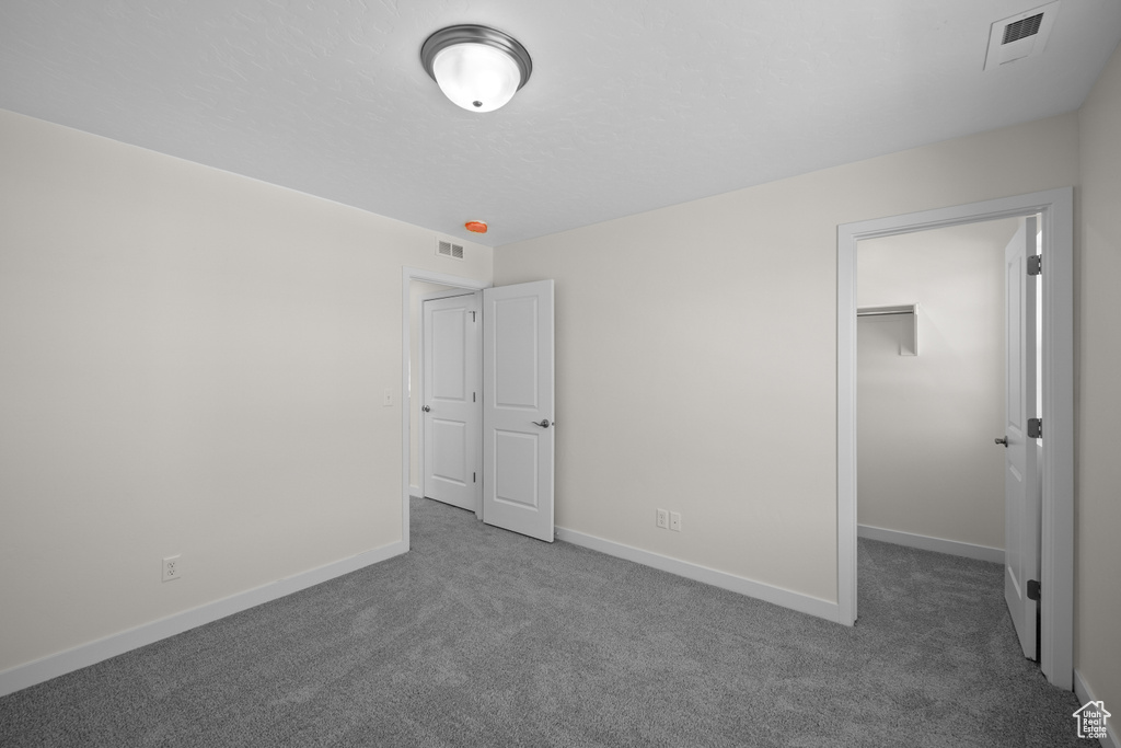 Unfurnished bedroom featuring dark colored carpet, a closet, and a walk in closet