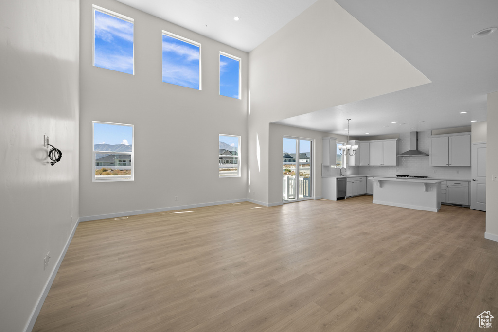 Unfurnished living room featuring light wood-type flooring, a chandelier, a high ceiling, and a healthy amount of sunlight