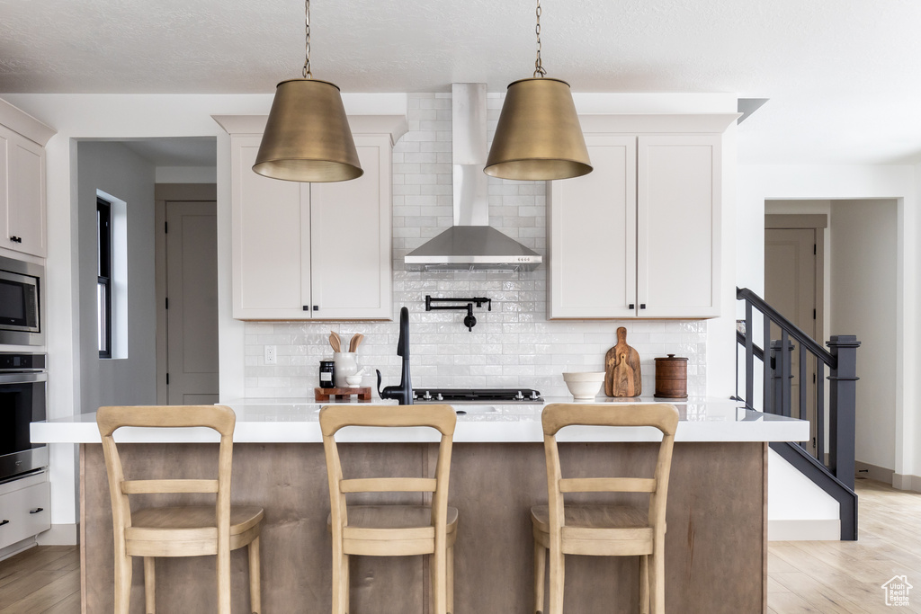 Kitchen featuring backsplash, wall chimney exhaust hood, light hardwood / wood-style flooring, and stainless steel appliances