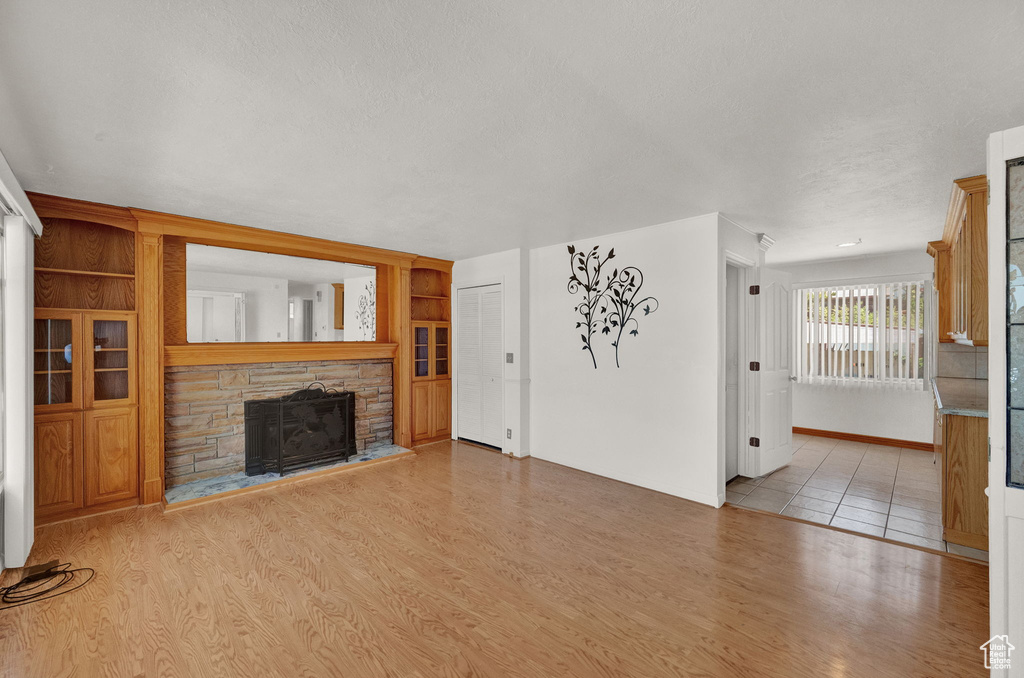 Unfurnished living room featuring a stone fireplace, built in features, and light tile floors