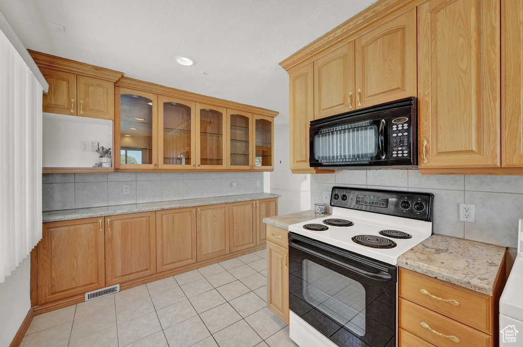 Kitchen with electric stove, light tile flooring, backsplash, and light stone countertops