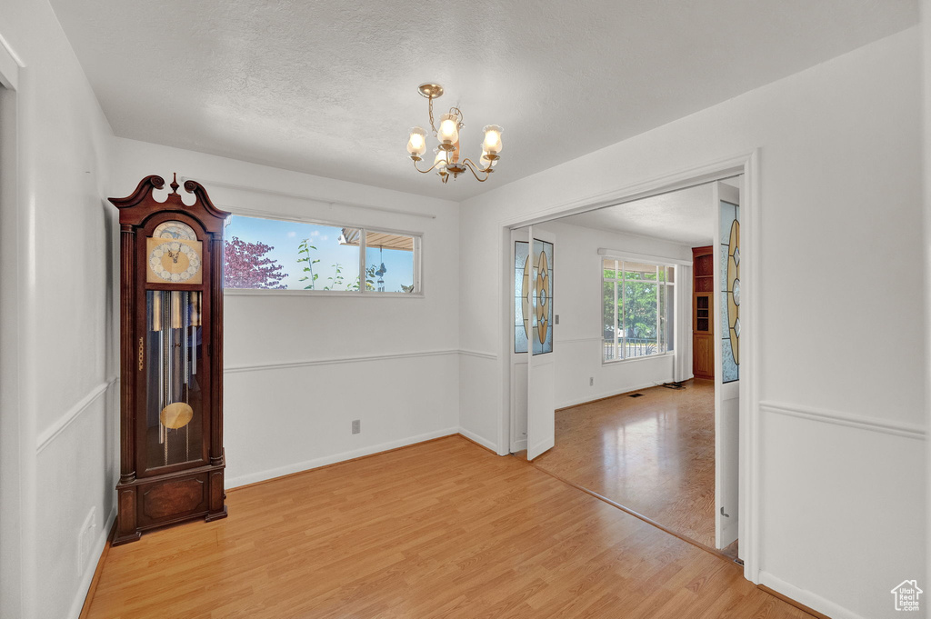 Empty room with light hardwood / wood-style flooring, a textured ceiling, and a chandelier