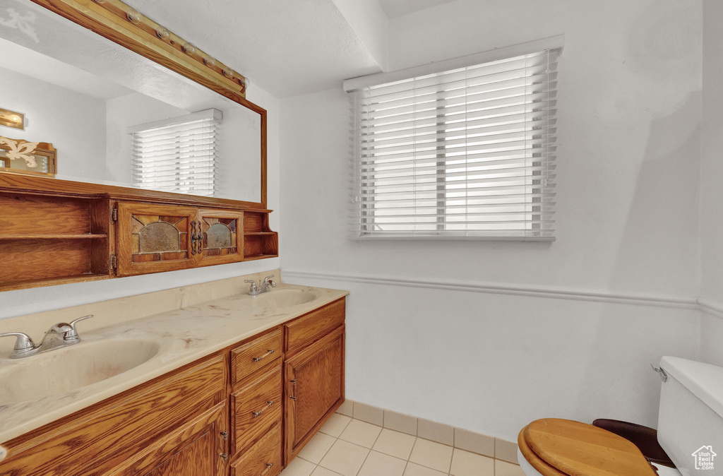 Bathroom featuring vanity with extensive cabinet space, double sink, toilet, and tile floors