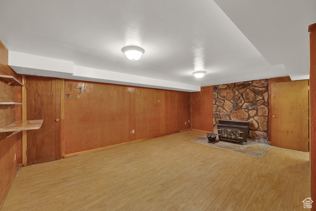 Unfurnished living room featuring wooden walls, light hardwood / wood-style floors, a stone fireplace, and a wood stove