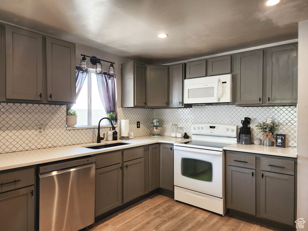 Kitchen featuring white appliances, sink, light hardwood / wood-style floors, and tasteful backsplash