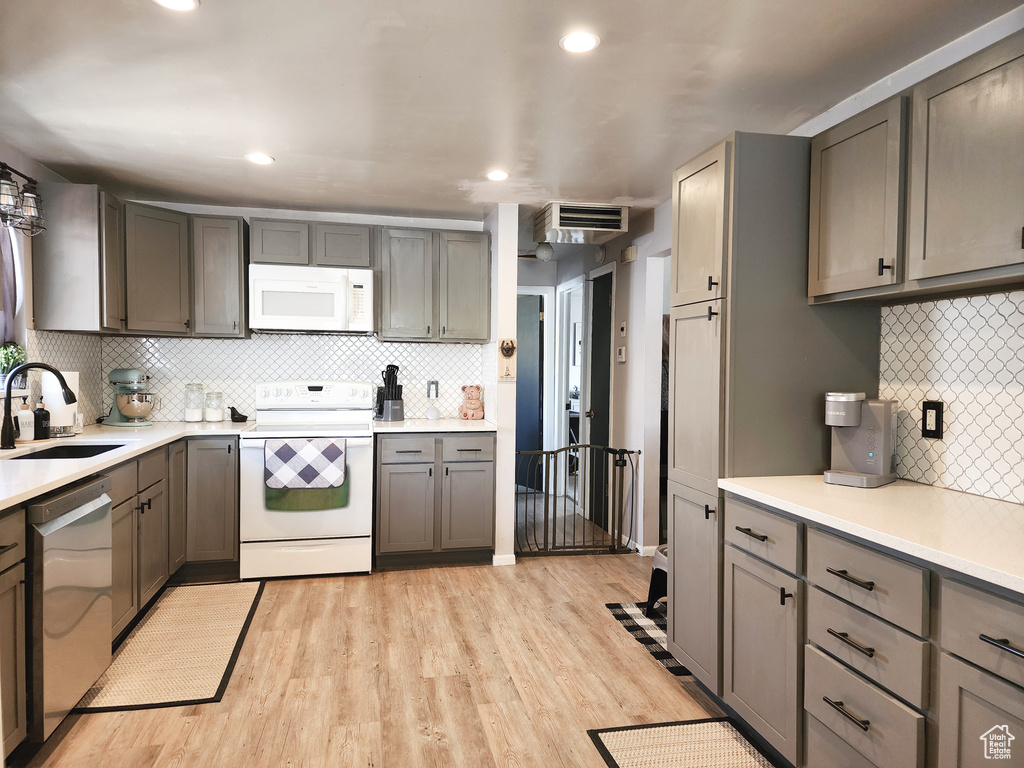 Kitchen with light hardwood / wood-style floors, white appliances, gray cabinets, backsplash, and sink
