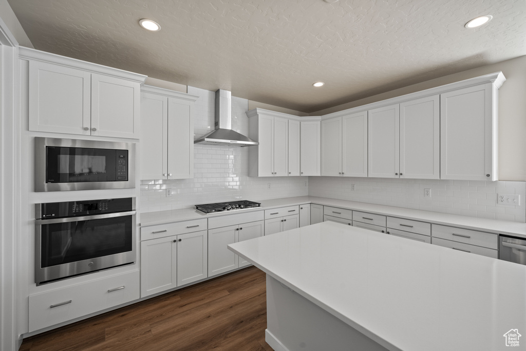 Kitchen with wall chimney exhaust hood, decorative backsplash, dark hardwood / wood-style flooring, stainless steel appliances, and white cabinets