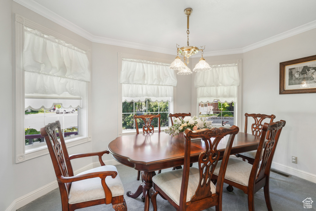 Carpeted dining space featuring a healthy amount of sunlight, ornamental molding, and an inviting chandelier