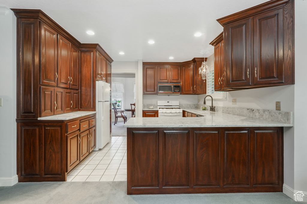 Kitchen featuring kitchen peninsula, white appliances, light stone counters, hanging light fixtures, and sink