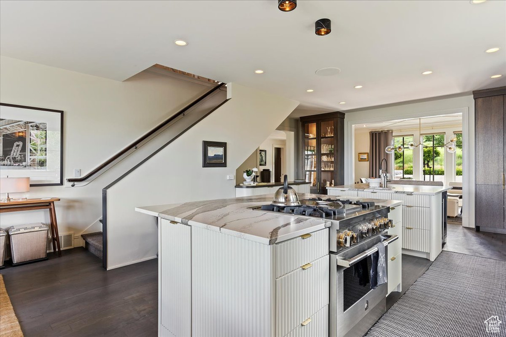 Kitchen with high end stainless steel range, white cabinetry, a center island, light stone countertops, and dark hardwood / wood-style flooring