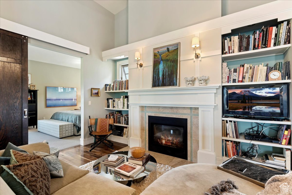 Living room with a high ceiling, a tiled fireplace, wood-type flooring, and built in shelves