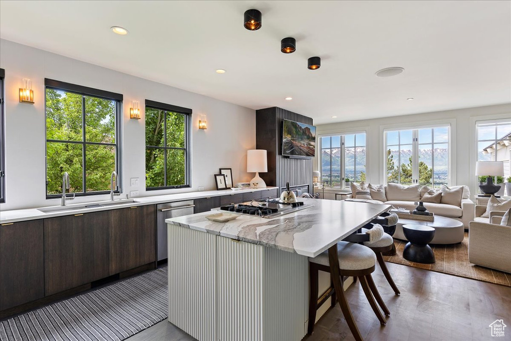 Kitchen featuring a kitchen breakfast bar, appliances with stainless steel finishes, hardwood / wood-style flooring, light stone counters, and dark brown cabinetry