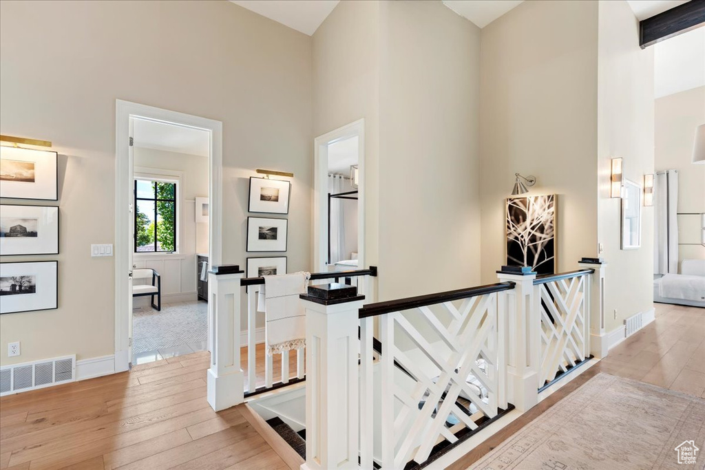 Corridor with beamed ceiling, a towering ceiling, and light hardwood / wood-style flooring