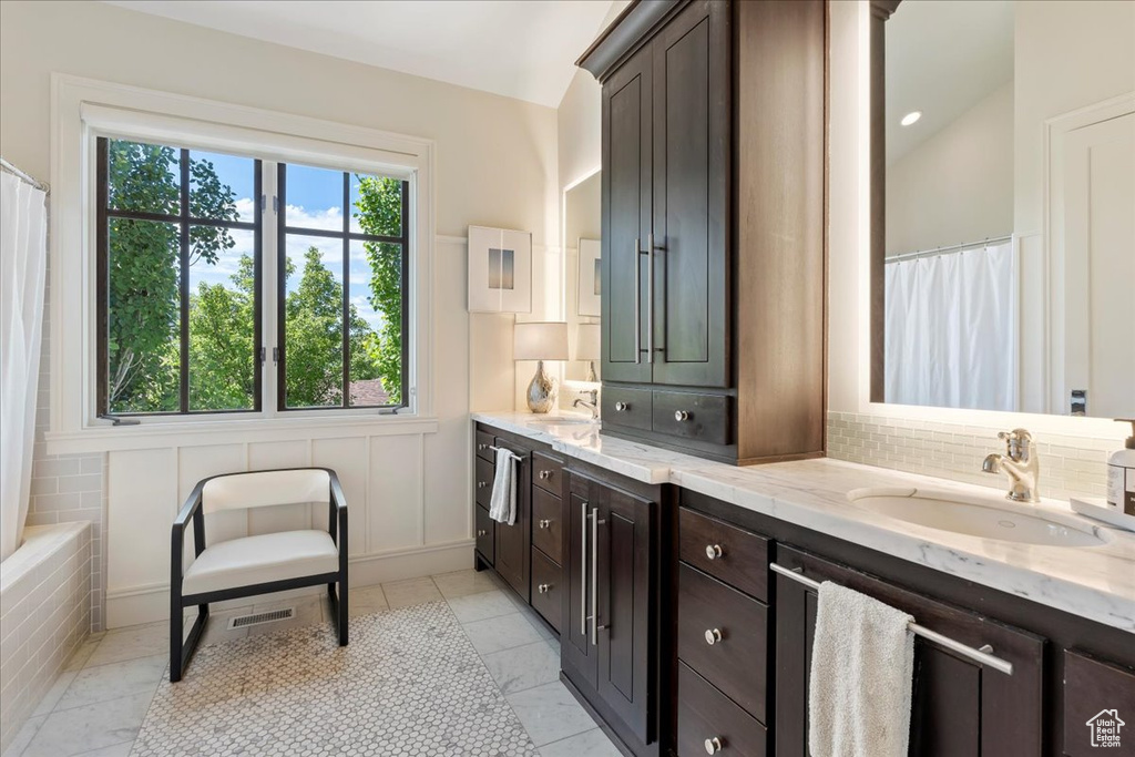 Bathroom featuring tile floors, tasteful backsplash, vaulted ceiling, and dual bowl vanity