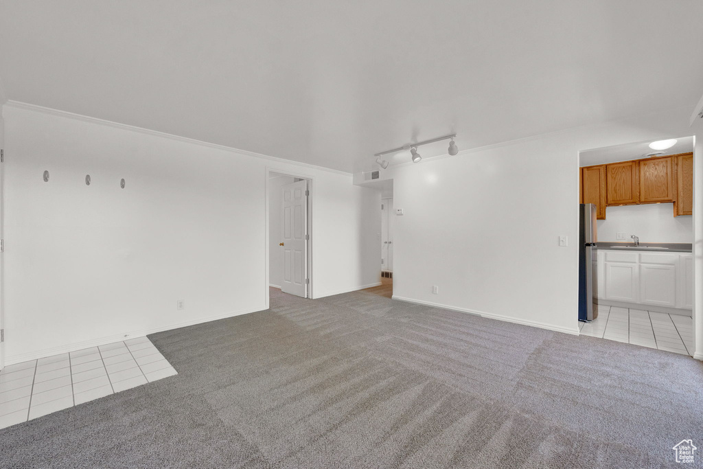 Unfurnished living room featuring crown molding, sink, light tile flooring, and track lighting