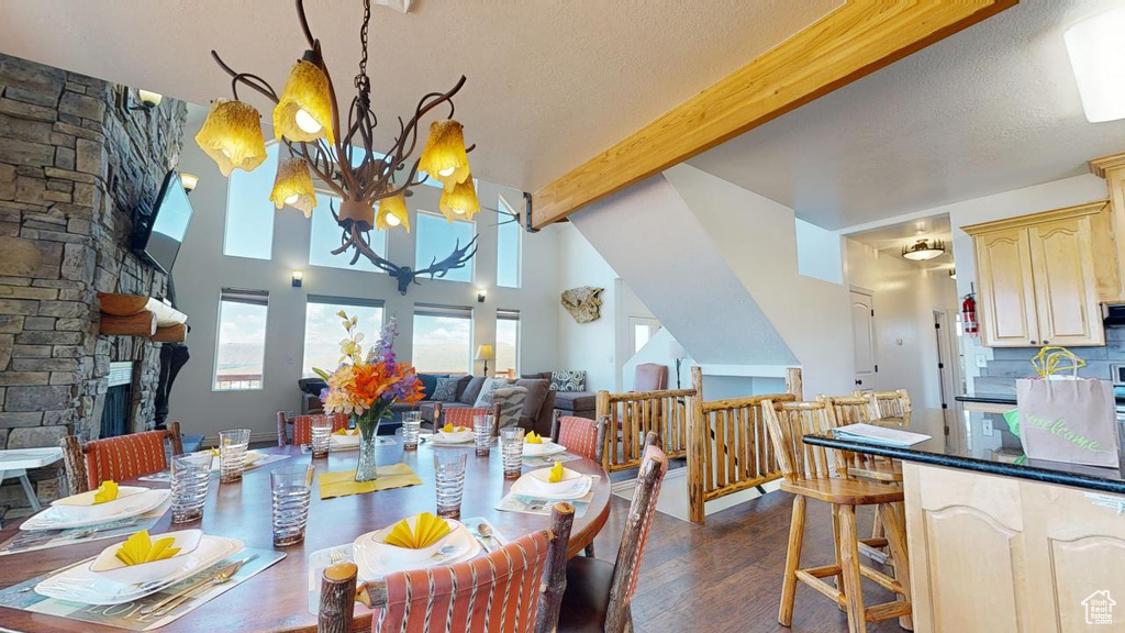 Dining space with beamed ceiling, a fireplace, an inviting chandelier, a textured ceiling, and dark hardwood / wood-style flooring