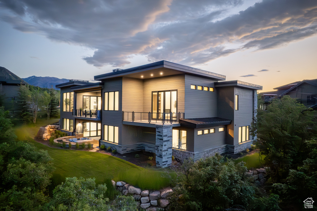 Back house at dusk featuring a mountain view, a balcony, and a lawn