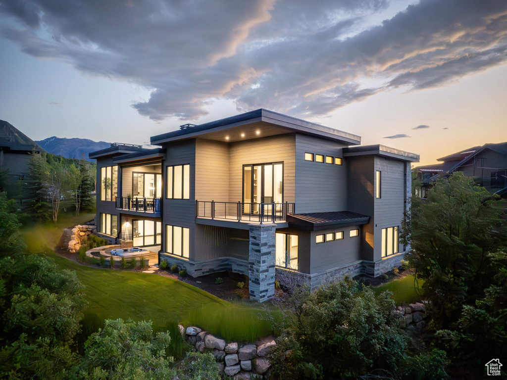 Back house at dusk with a mountain view, a balcony, and a lawn