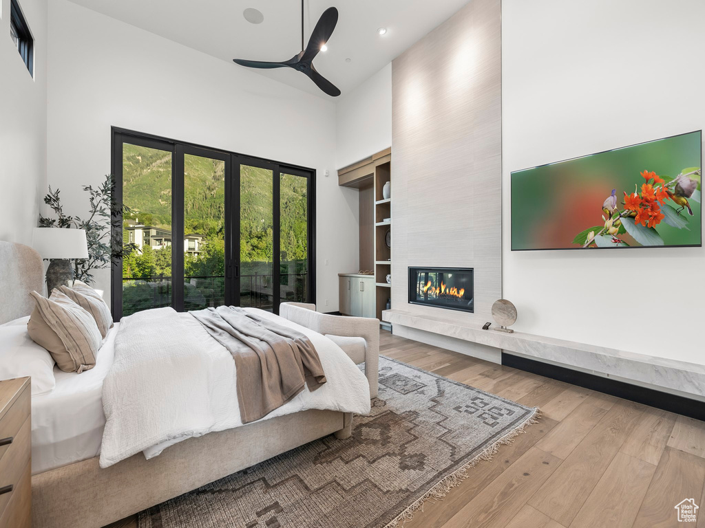 Bedroom featuring a high ceiling, a fireplace, wood-type flooring, and ceiling fan