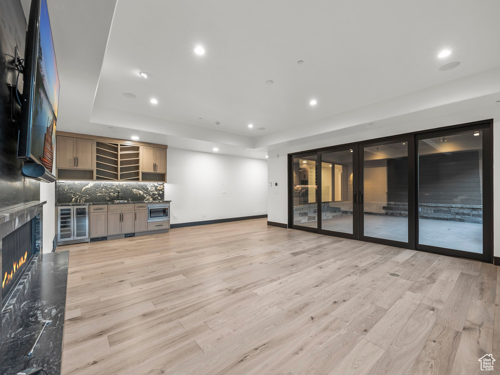 Unfurnished living room featuring a premium fireplace, wine cooler, a raised ceiling, and light hardwood / wood-style flooring