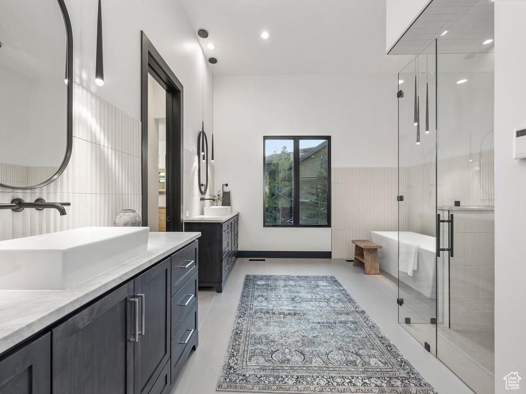 Bathroom featuring a shower with door, tile flooring, dual bowl vanity, and tile walls