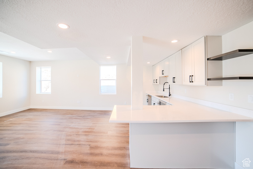 Kitchen with white cabinetry, kitchen peninsula, light wood-type flooring, a textured ceiling, and sink