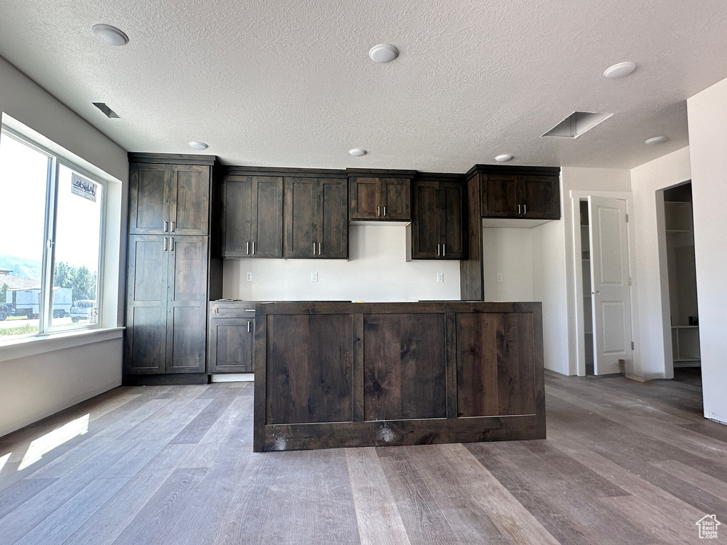 Kitchen with a textured ceiling, light wood-type flooring, and dark brown cabinets