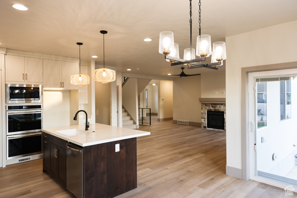 Kitchen featuring decorative light fixtures, an island with sink, sink, a stone fireplace, and light hardwood / wood-style floors