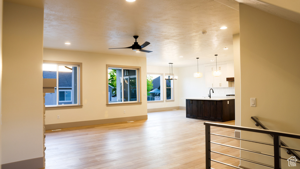 Living room featuring sink, a textured ceiling, ceiling fan with notable chandelier, and light wood-type flooring