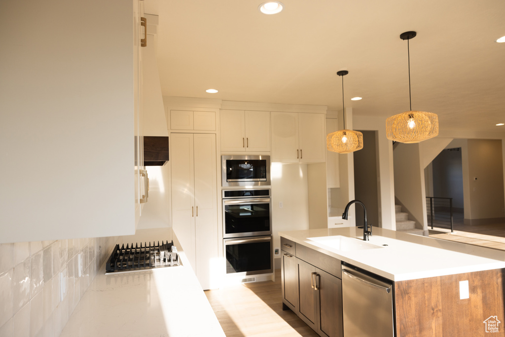 Kitchen with sink, white cabinetry, stainless steel appliances, decorative light fixtures, and a kitchen island with sink