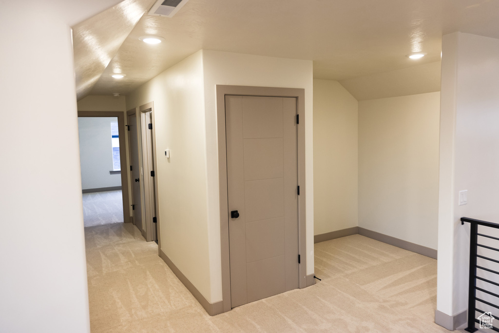 Hallway with light colored carpet and vaulted ceiling