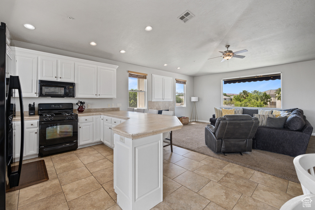 Kitchen featuring white cabinetry, black appliances, kitchen peninsula, ceiling fan, and light tile floors