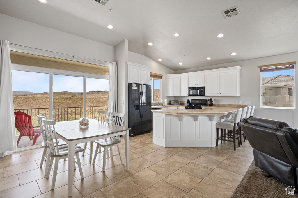 Kitchen with white cabinets, black appliances, light tile floors, and lofted ceiling