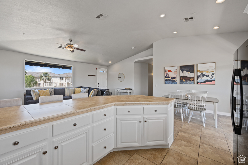 Kitchen with white cabinetry, lofted ceiling, black refrigerator, ceiling fan, and light tile floors