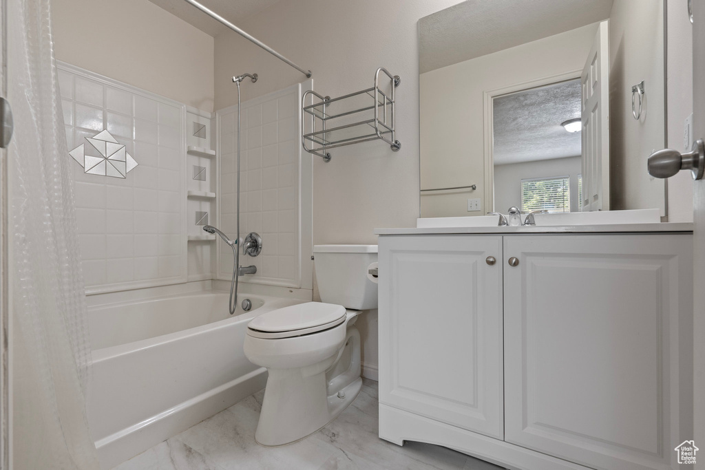 Full bathroom featuring toilet, tile flooring, shower / tub combo, vanity, and a textured ceiling