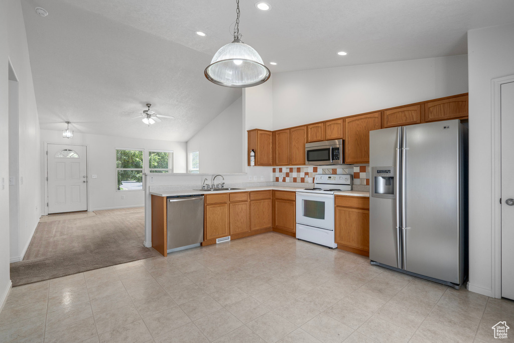 Kitchen featuring appliances with stainless steel finishes, light carpet, kitchen peninsula, pendant lighting, and sink