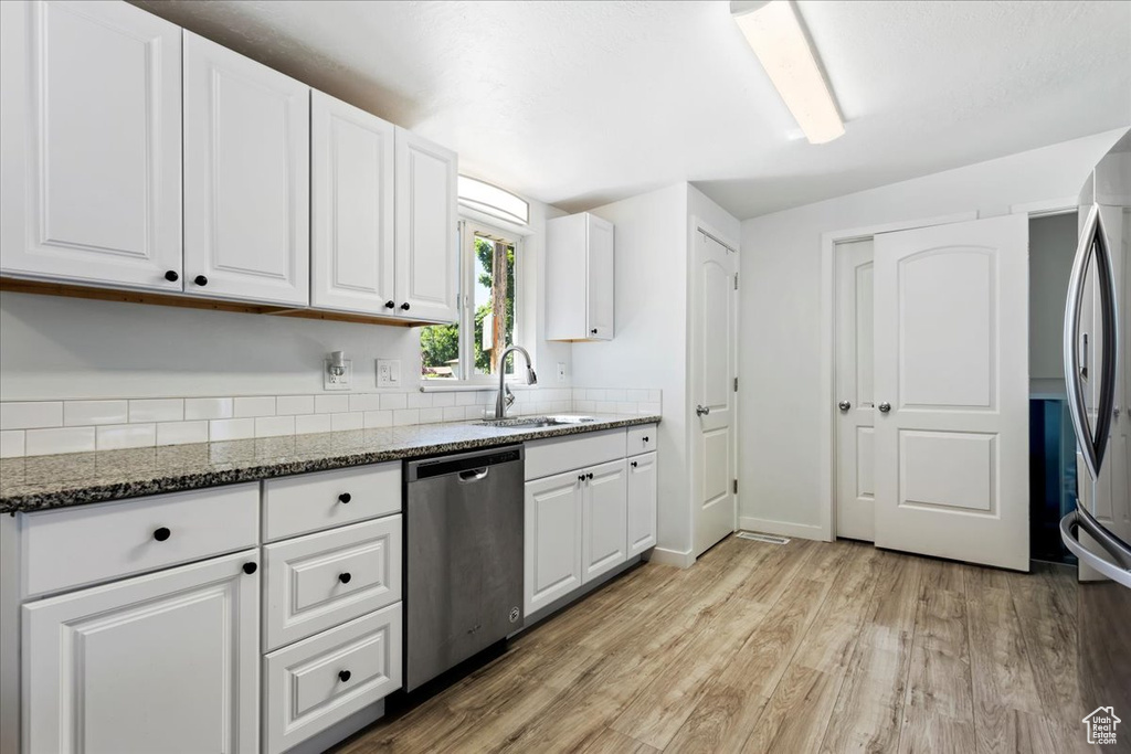 Kitchen featuring dark stone counters, light hardwood / wood-style floors, stainless steel appliances, white cabinets, and sink