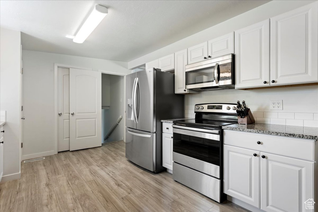 Kitchen with white cabinets, appliances with stainless steel finishes, stone counters, and light hardwood / wood-style flooring