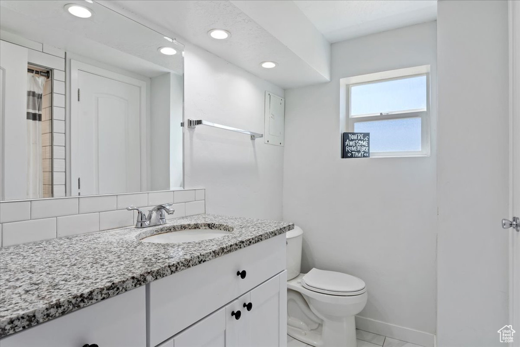 Bathroom with backsplash, vanity with extensive cabinet space, toilet, and tile floors