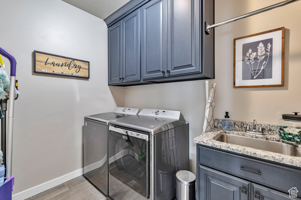 Clothes washing area featuring washing machine and dryer, sink, light wood-type flooring, and cabinets