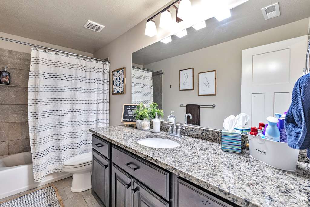 Full bathroom with toilet, tile floors, large vanity, shower / bath combo with shower curtain, and a textured ceiling