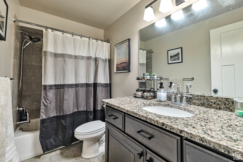 Full bathroom featuring a textured ceiling, shower / bath combo with shower curtain, tile floors, oversized vanity, and toilet