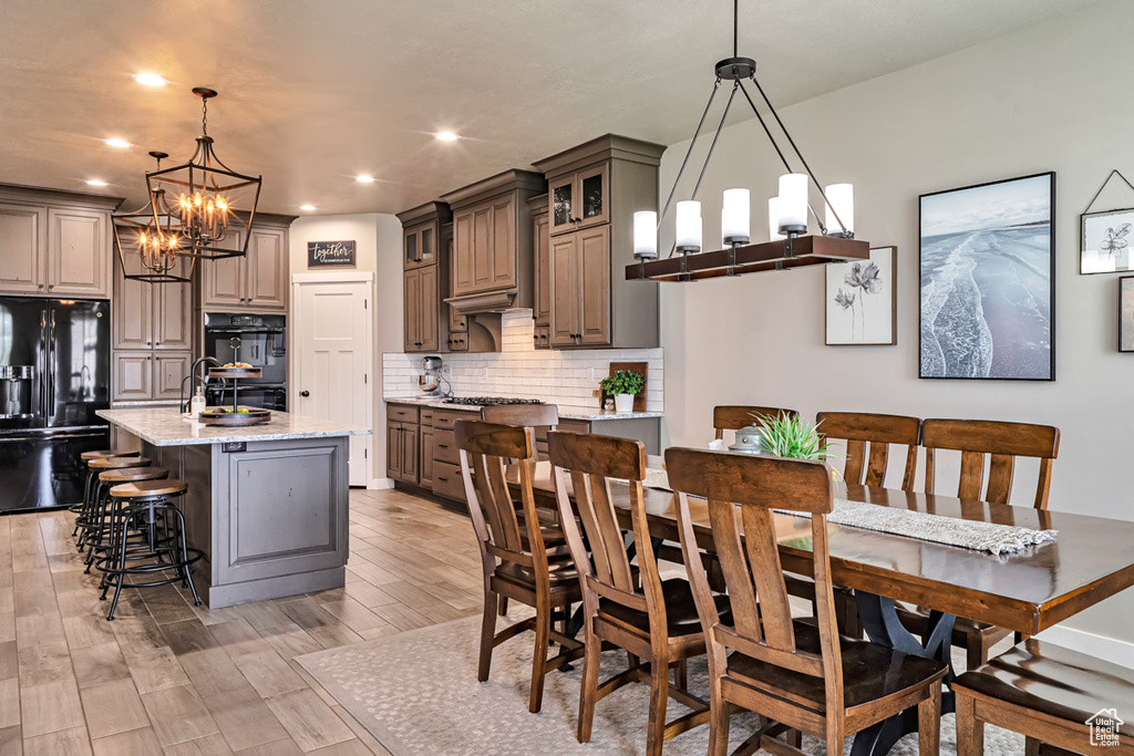 Kitchen with a center island with sink, black appliances, hardwood / wood-style flooring, light stone counters, and tasteful backsplash