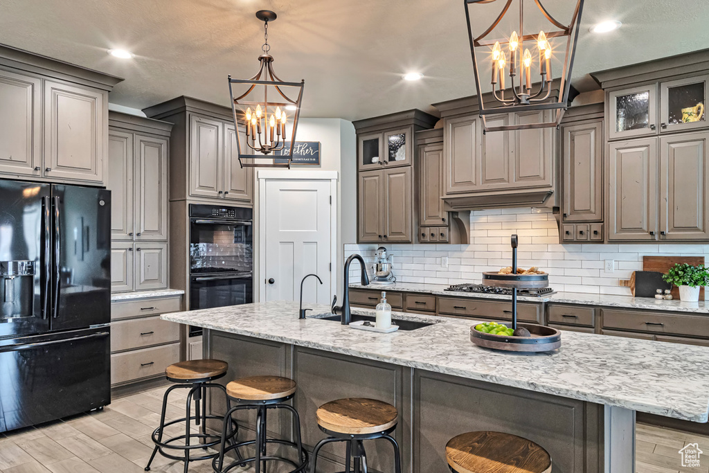 Kitchen with light hardwood / wood-style flooring, tasteful backsplash, a center island with sink, black appliances, and hanging light fixtures